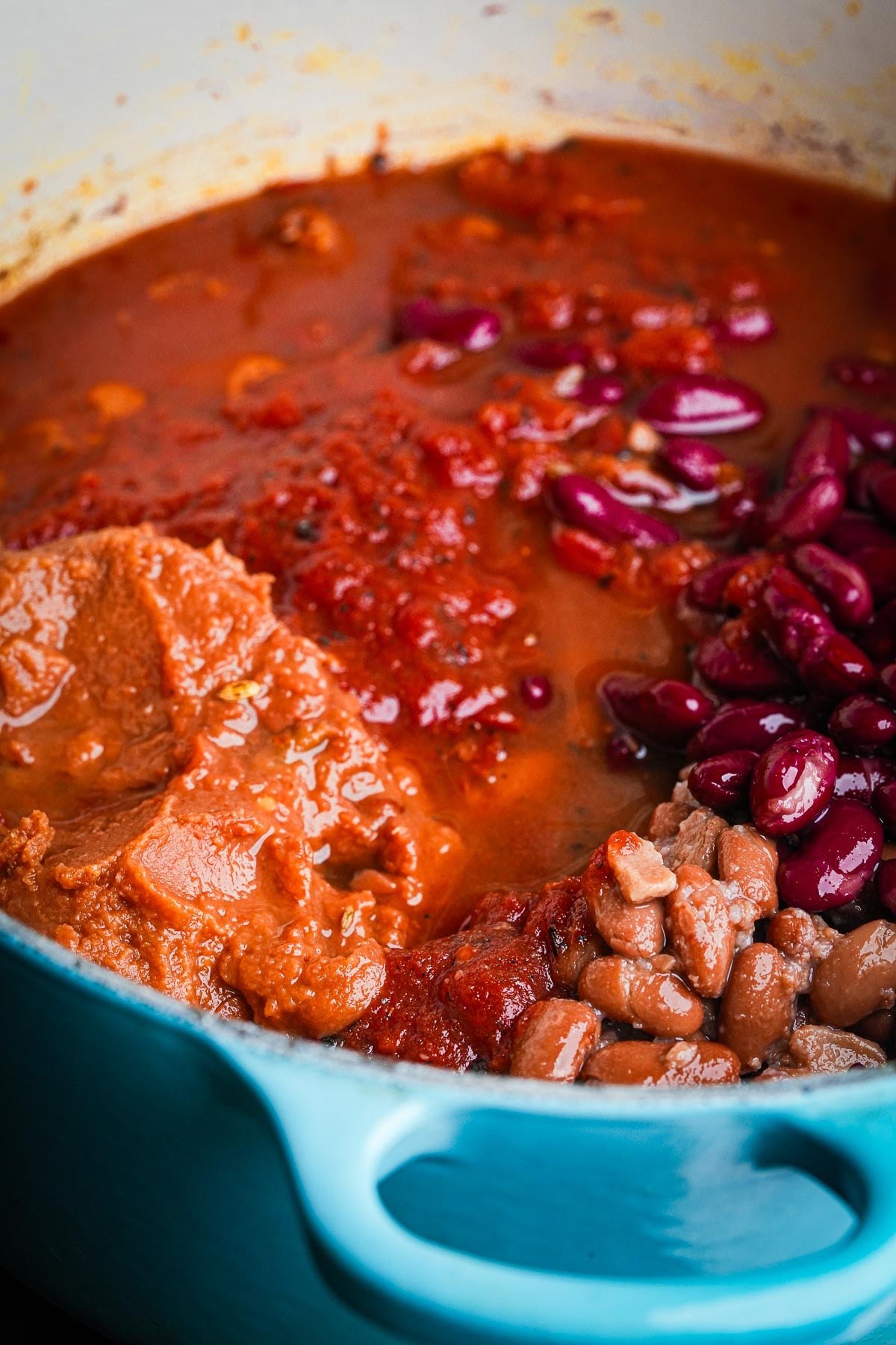 A close-up of a pot containing a mixture of red kidney beans, pinto beans, tomato sauce, and other ingredients being cooked together to make vegan chili to serve in a hat.