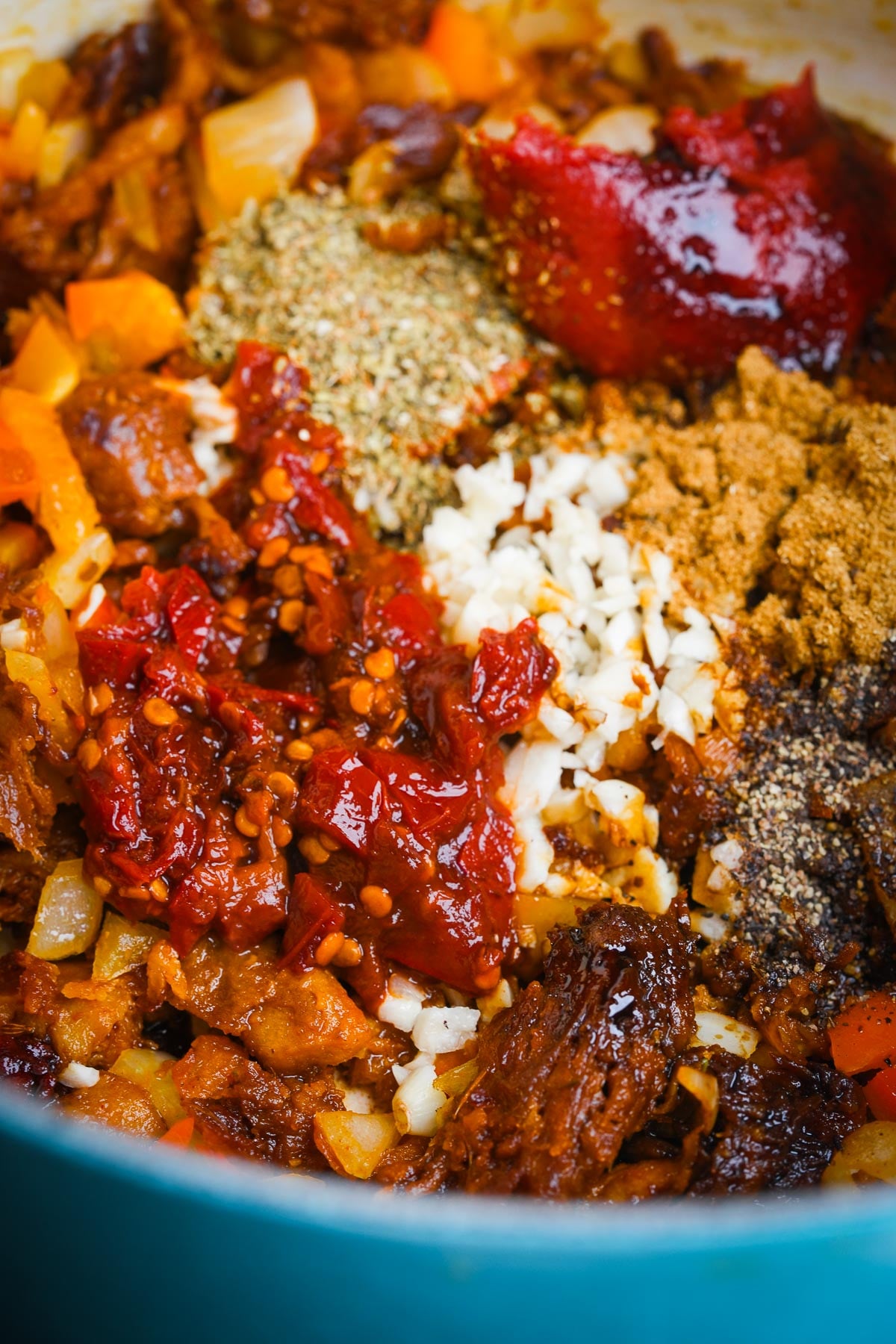 A pot filled with various ingredients for chili, including chunks of vegan meat, chopped onions, tomatoes, garlic, and assorted spices.