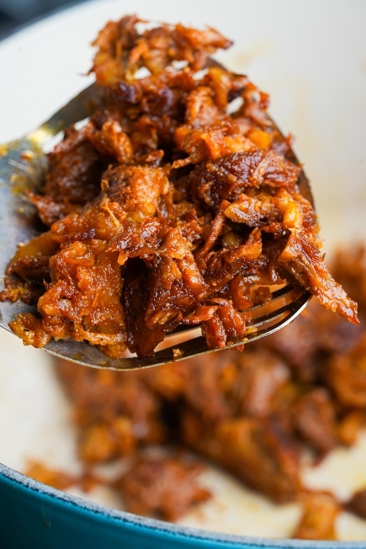 A close-up of shredded seitan being held on a spatula over dutch oven.