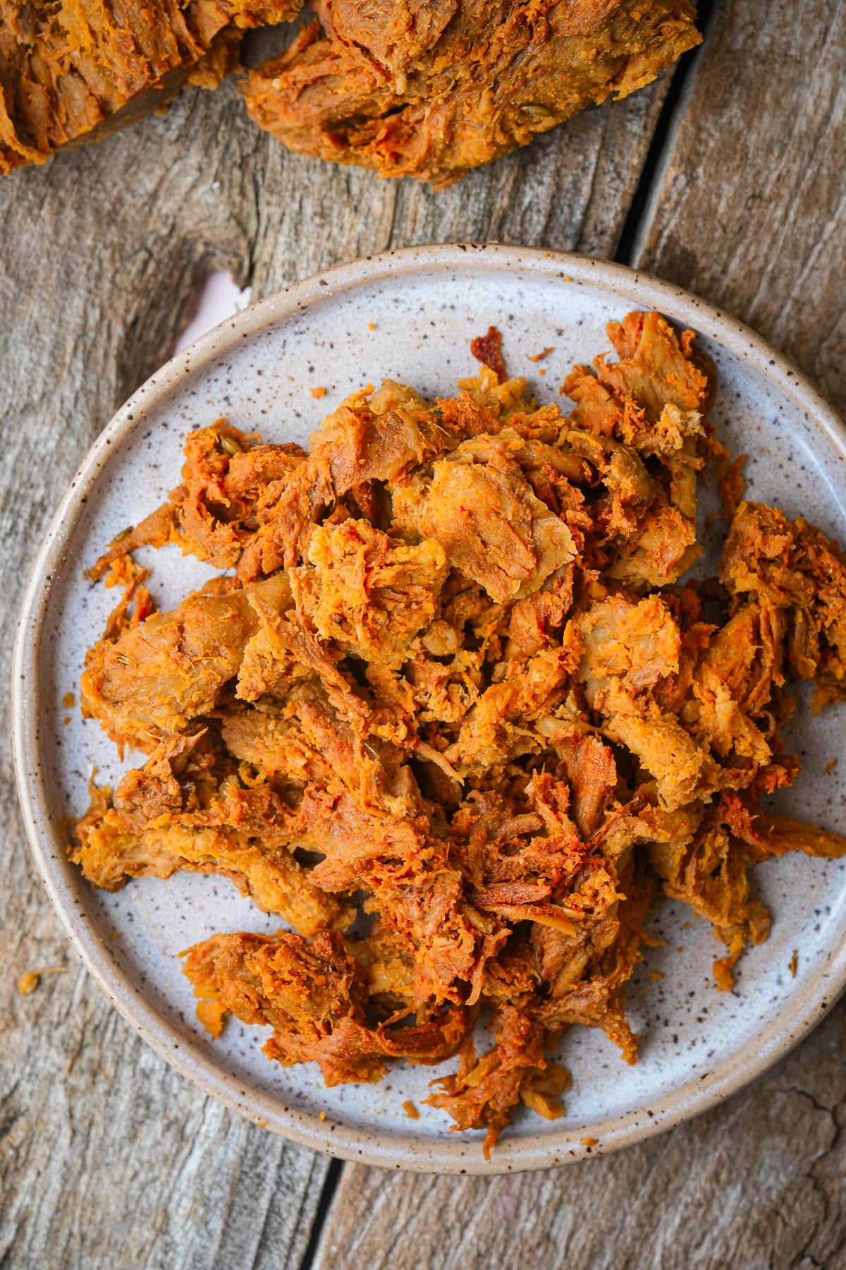 A plate of shredded, seasoned seitan on a wooden surface.