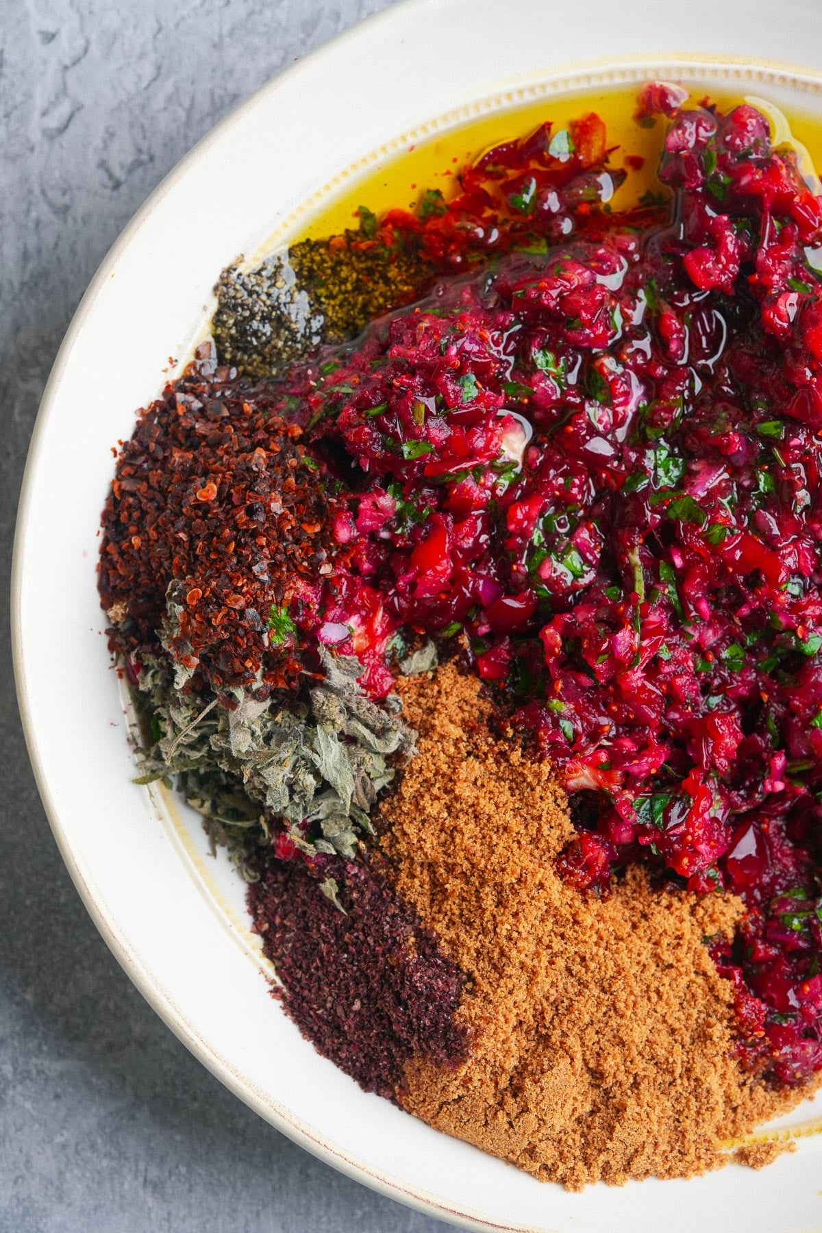 A plate with various spices and chopped herbs, including Aleppo pepper flakes, dried herbs, ground spices, and a mixture of drained ground cranberries and onions.