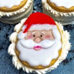 A cookie decorated with a Santa Claus face, featuring white icing for the beard and a red hat.