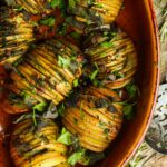 Sliced hasselback potatoes with herbs and spices in a baking dish.