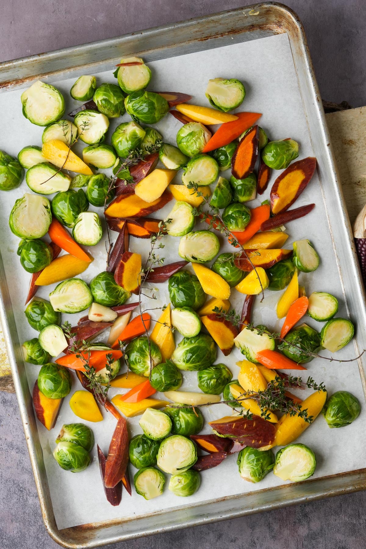 Colorful sliced Brussels sprouts and multicolor carrots, are arranged on a baking sheet lined with parchment paper.