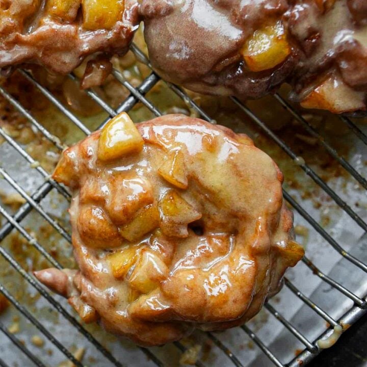 Close-up of glazed apple fritters with chunks of apple on a metal cooling rack.