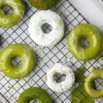 Green and white glazed donuts on a cooling rack, some topped with powdered sugar and others with a green glaze.