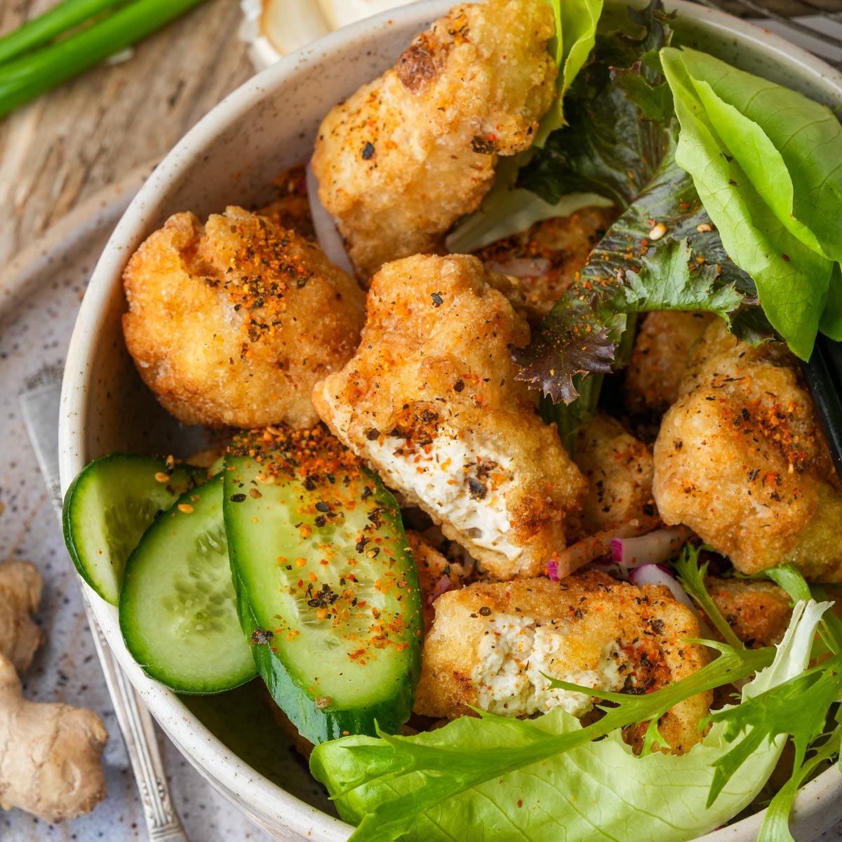 A bowl of fried tofu karaage with sliced cucumbers and mixed greens, garnished with spices.
