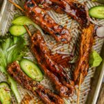 Skewered vegan yakitori with glossy tare sauce on a tray, garnished with cucumber slices and lettuce.