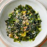 A bowl of wakame salad topped with sesame seeds and sliced green onions.