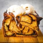 Close-up of a vegan chocolate babka topped with two scoops of vanilla ice cream, sitting on a wooden surface.