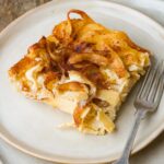 A slice of vegan noodle kugel with cinnamon on a plate, accompanied by a fork.