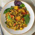 A plate of green curry fried rice with tofu, peas, red bell peppers, and fresh herbs on a round white dish.
