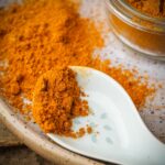 A ceramic spoon holds ground Japanese curry powder on a plate, with more turmeric scattered around and a jar partially visible.