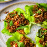 Tofu larb salad filled with spicy browned tofu, garnished with herbs and sliced red chilies, served on a speckled plate.