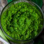 A bowl of vegan green curry paste on a rustic wooden surface, accompanied by fresh green onions.