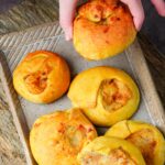 Hand picking a freshly baked vegan knish from a plate.