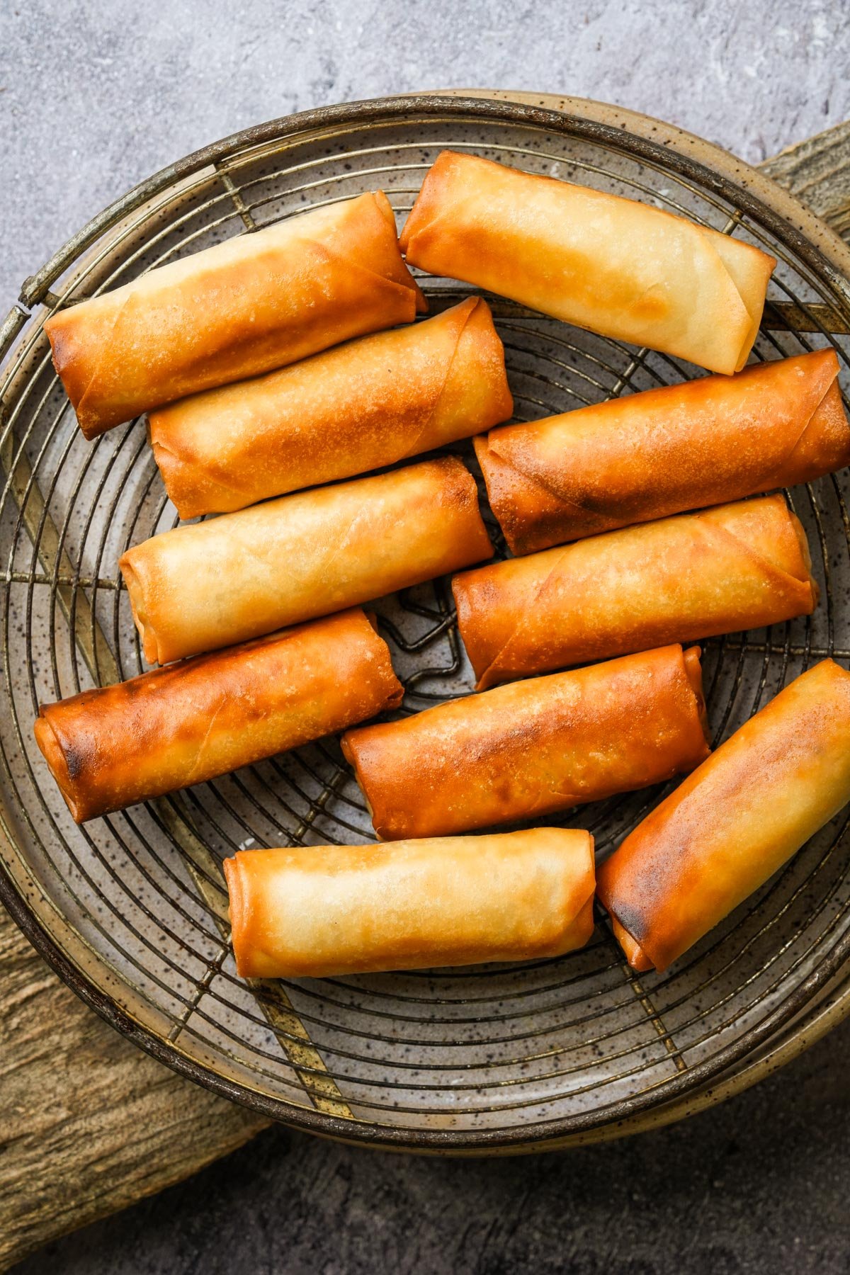 Golden brown spring rolls arranged on a round wire rack over a wooden surface.