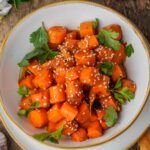 A bowl of Moroccan carrot salad garnished with sesame seeds and fresh parsley, served on a white plate.