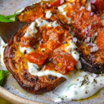 Borani banjan topped with tomato sauce, chopped red onion, herbs, and a creamy herbed yogurt on a plate.