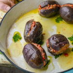 Four stuffed makdous with a walnut and pepper-based filling are arranged in a baking dish with olive oil and parsley leaves.