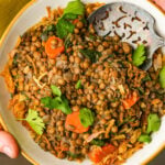 A bowl of cooked Moroccan lentils with carrots, greens, and herbs, served with a metal slotted spoon.