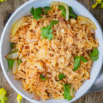 A white bowl filled with seasoned Turkish rice, garnished with caramelized onions and fresh parsley, placed on a wooden surface.