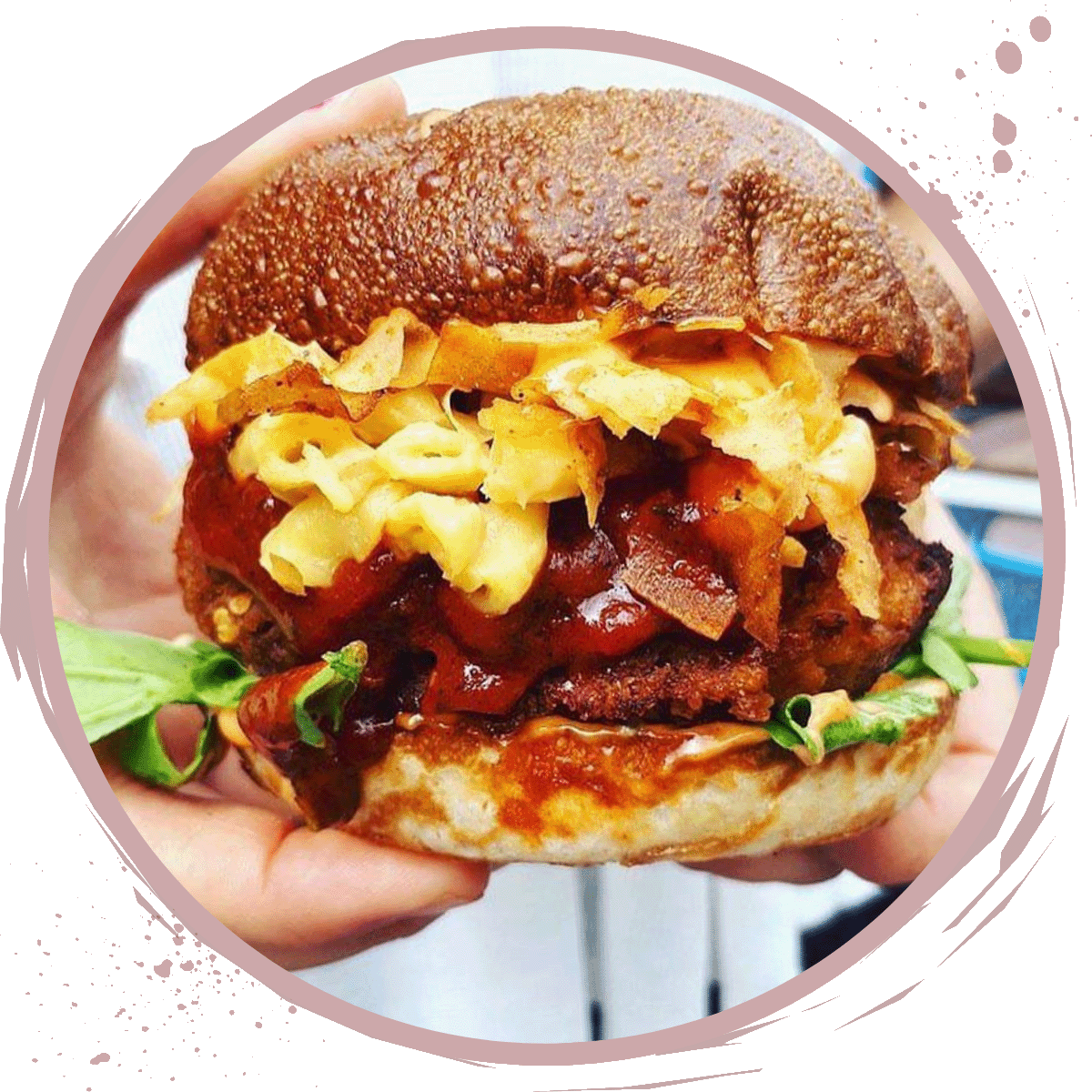 A close-up of hands holding a large burger with a beef patty, lettuce, barbecue sauce, macaroni and cheese, crispy onions, and a toasted bun-perfect inspiration for your next Tofu Cooking Class creation.
