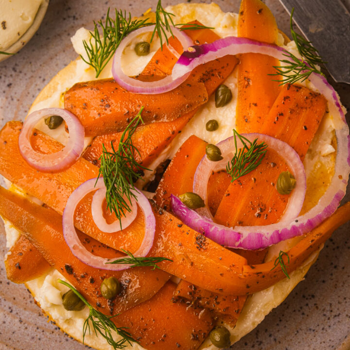 A plate with a bagel topped with cream cheese, carrot lox, red onion rings, capers, and fresh dill.