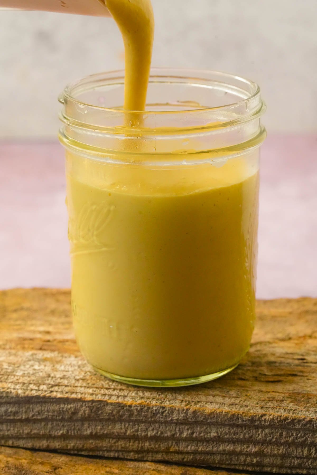 Homemade Just Egg is being poured into a glass mason jar sitting on a wooden surface.