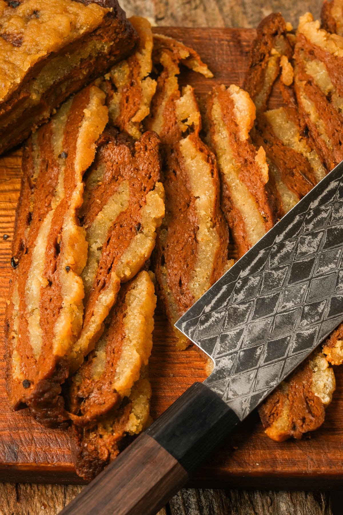 Sliced marbled seitan bacon on a wooden cutting board with a patterned chef’s knife next to the slices.