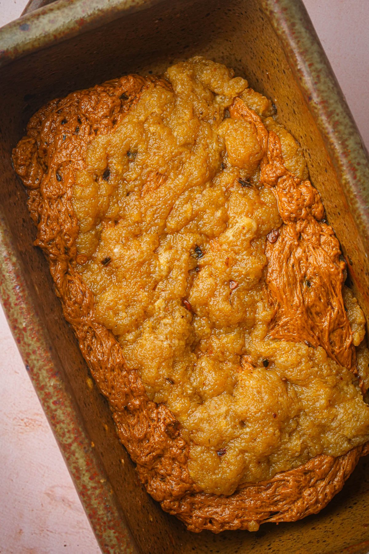 A close-up of unbaked seitan bacon dough with a rough, uneven surface in a rectangular metal baking pan.