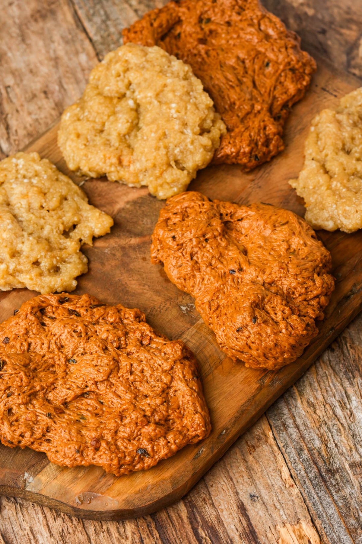 Several pieces of seitan bacon dough, and "fat" are flattened on a wooden cutting board.
