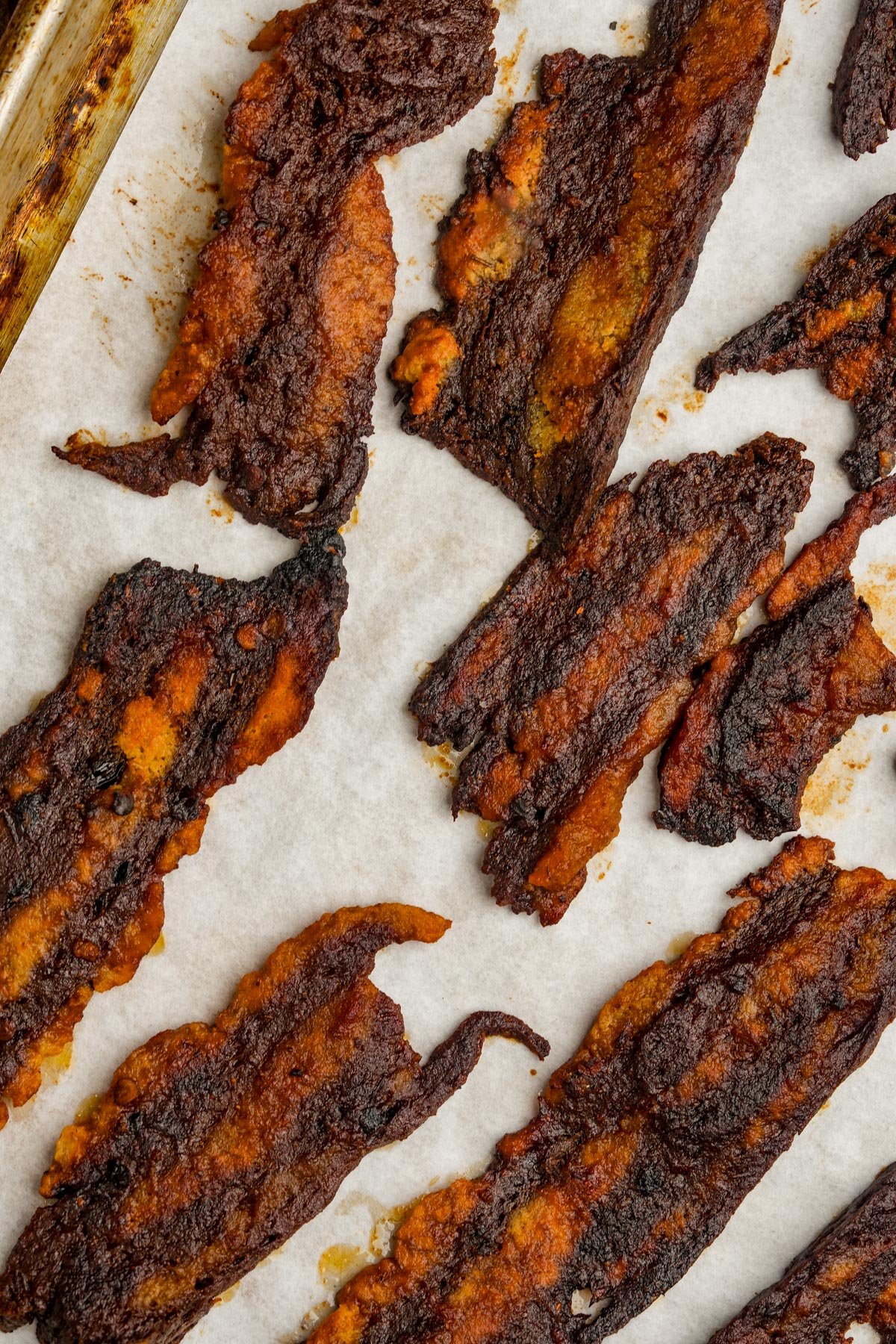Several strips of cooked seitan bacon on a parchment-lined baking sheet.