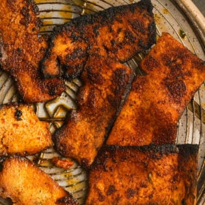 Several pieces of cooked, seasoned tofu bacon with charred edges are arranged on a round metal plate with visible oil and seasoning residue.