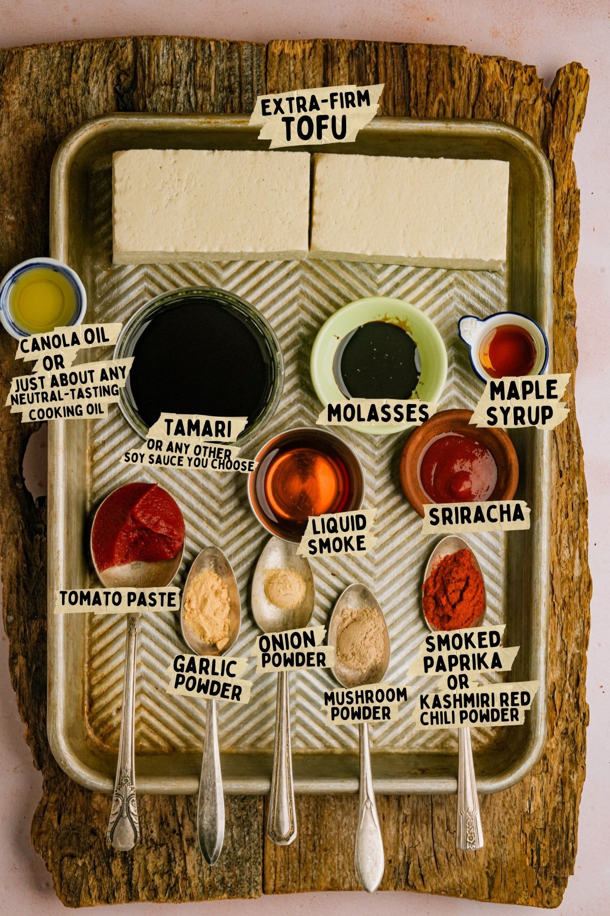 A tray with ingredients for a tofu bacon recipe: extra-firm tofu blocks and bowls of canola oil, tamari, molasses, maple syrup, tomato paste, sriracha, liquid smoke, and spoons of garlic, onion, mushroom, and chili powders.