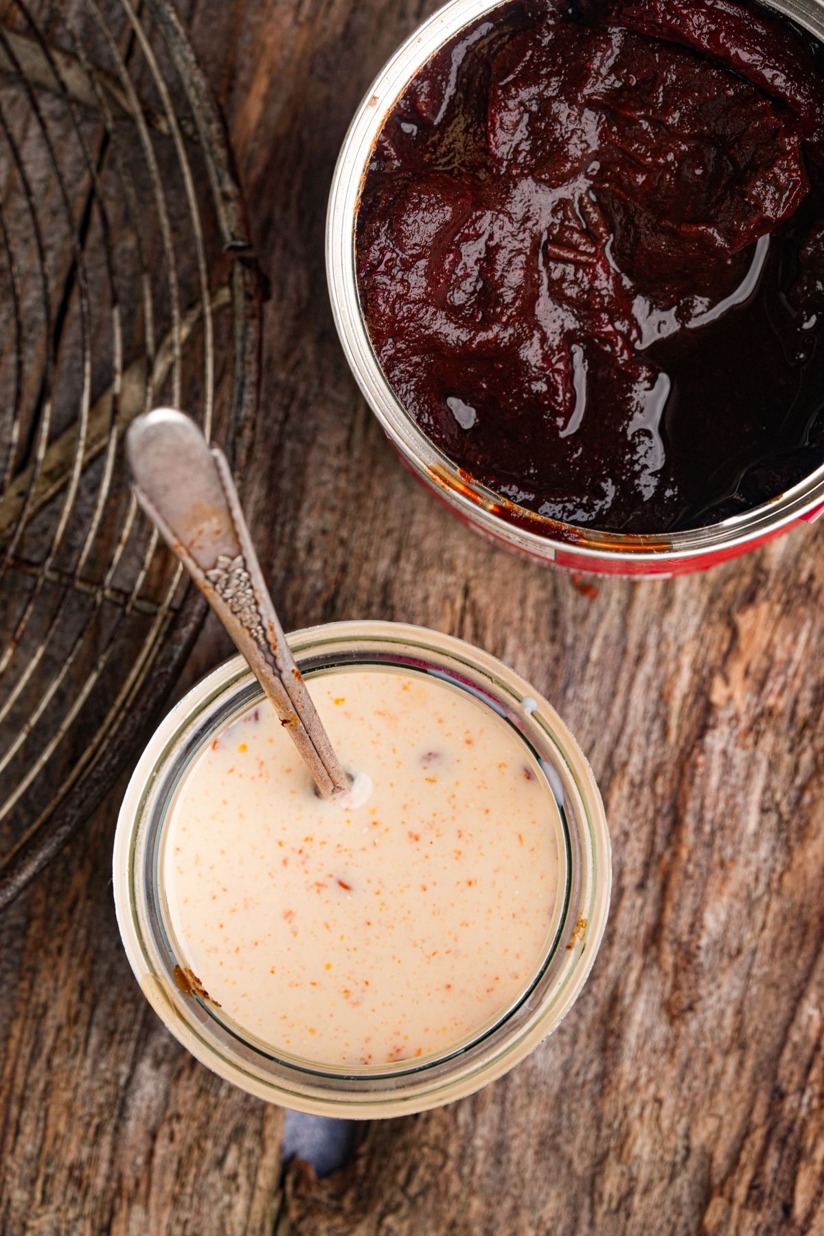A jar of chipotle infused plant-milk and a spoon beside an open can of chipotle peppers in adobo on a wooden surface.