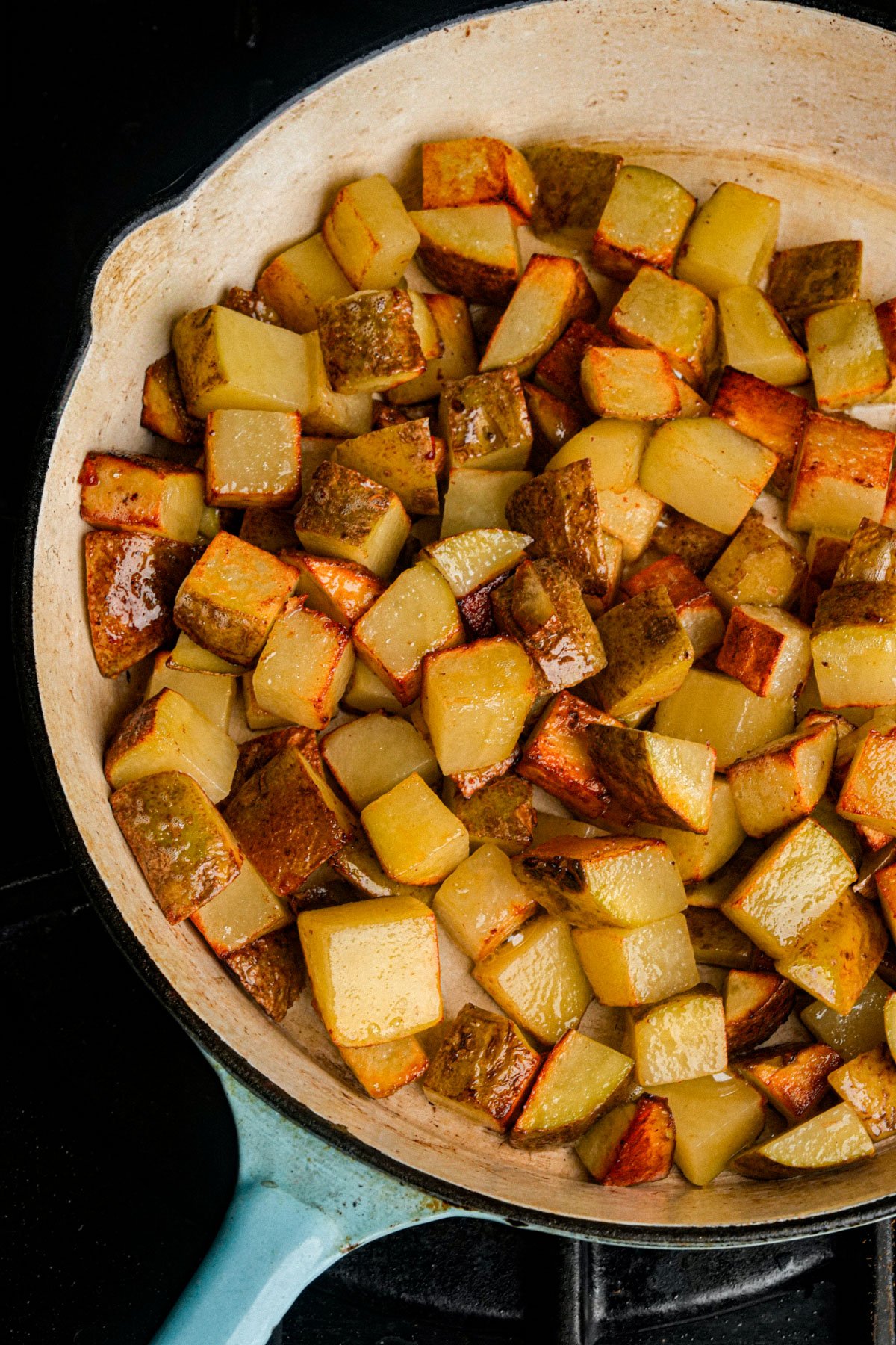 A skillet filled with evenly browned, diced roasted potatoes, showing crispy edges and a mix of golden and darker brown pieces.