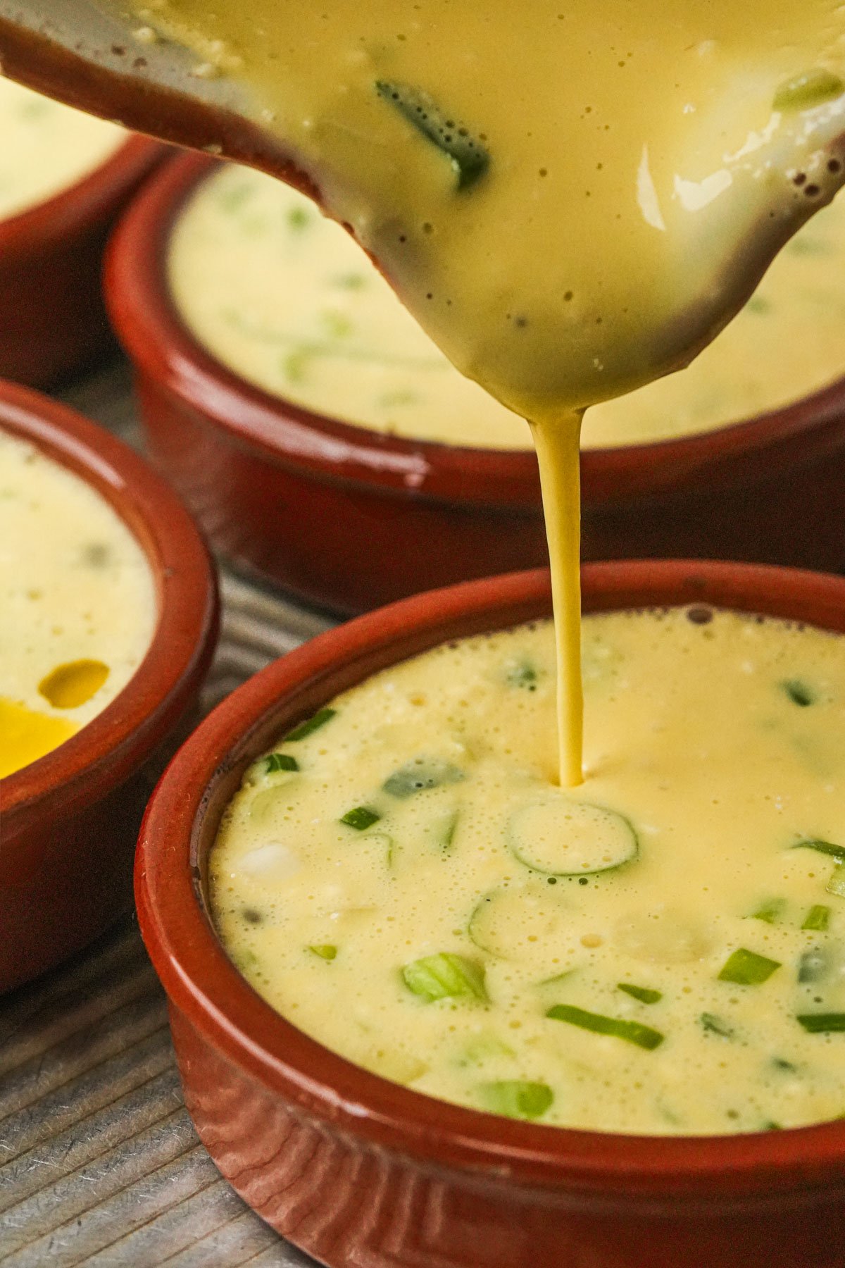 Just Egg mixture being poured into a small brown ramekin with similar dishes in the background.