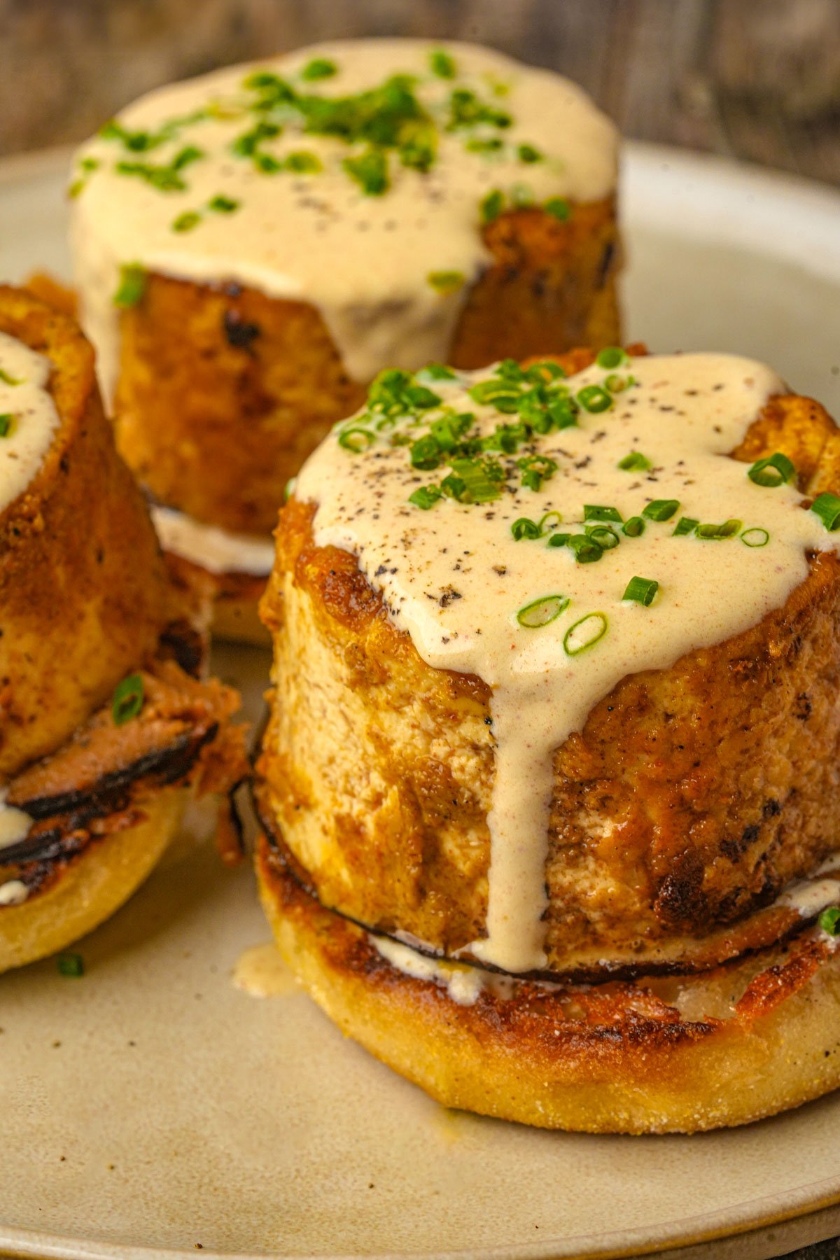 Servings of vegan eggs benedict topped with creamy sauce and chopped chives, served on a beige plate.