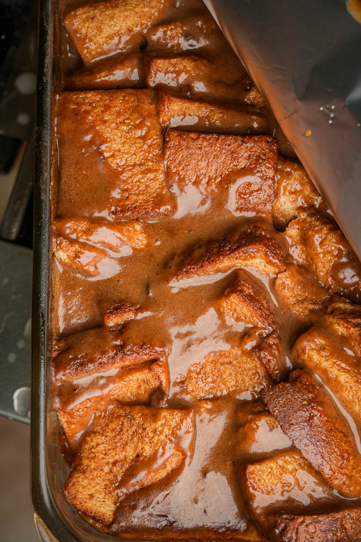 A partially baked vegan French toast casserole in a glass dish, covered with aluminum foil.