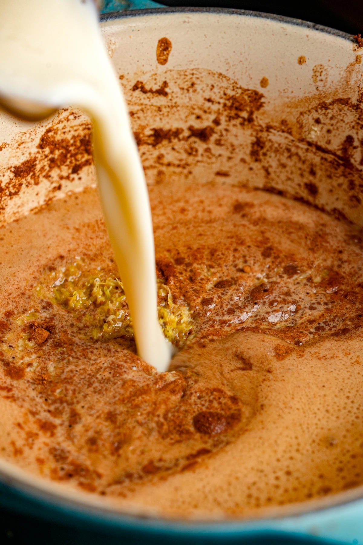Vegan milk is being poured into a pot containing a frothy, brown spiced custard for vegan French toast casserole.