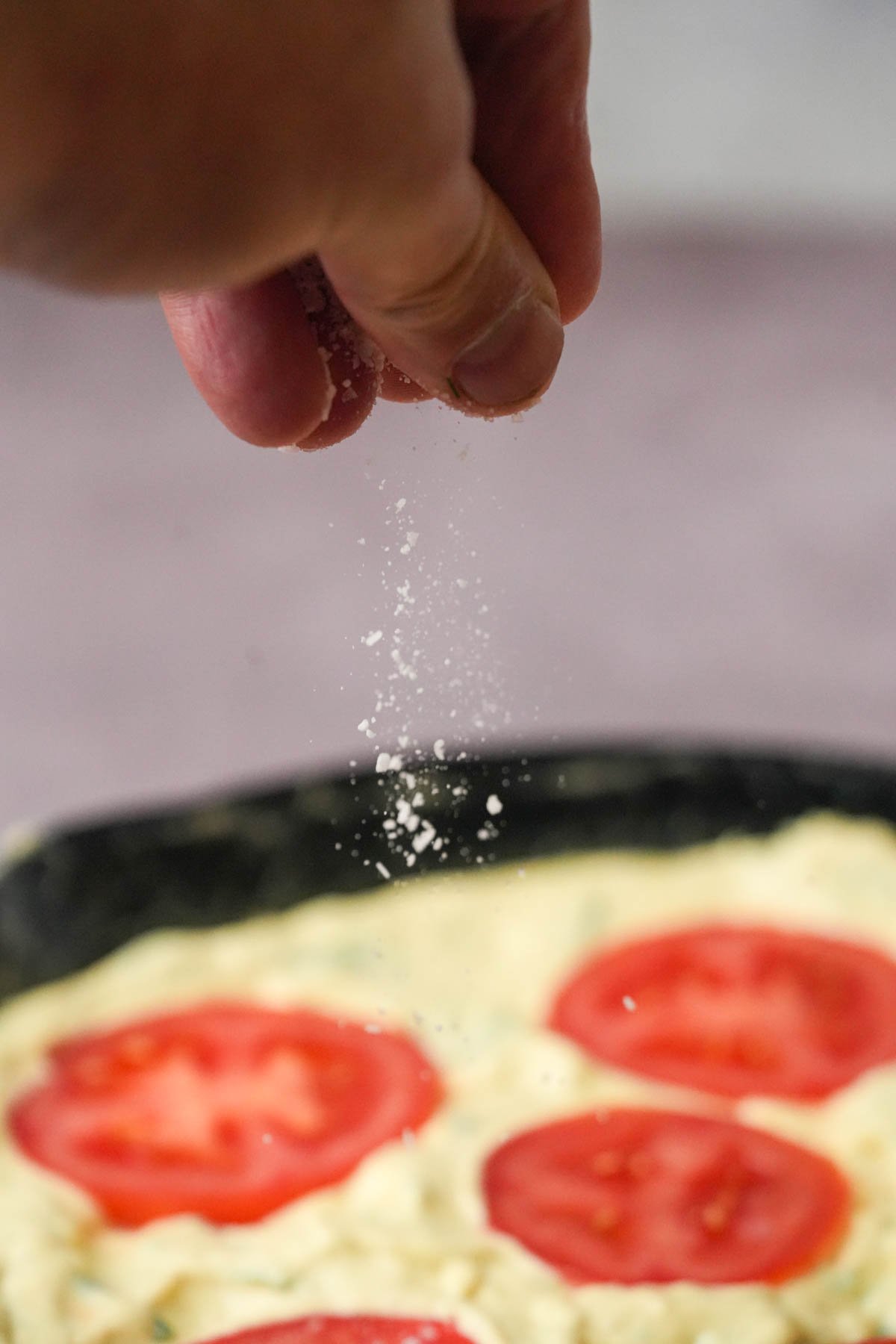 A hand sprinkles salt over an unbaked vegan frittata.