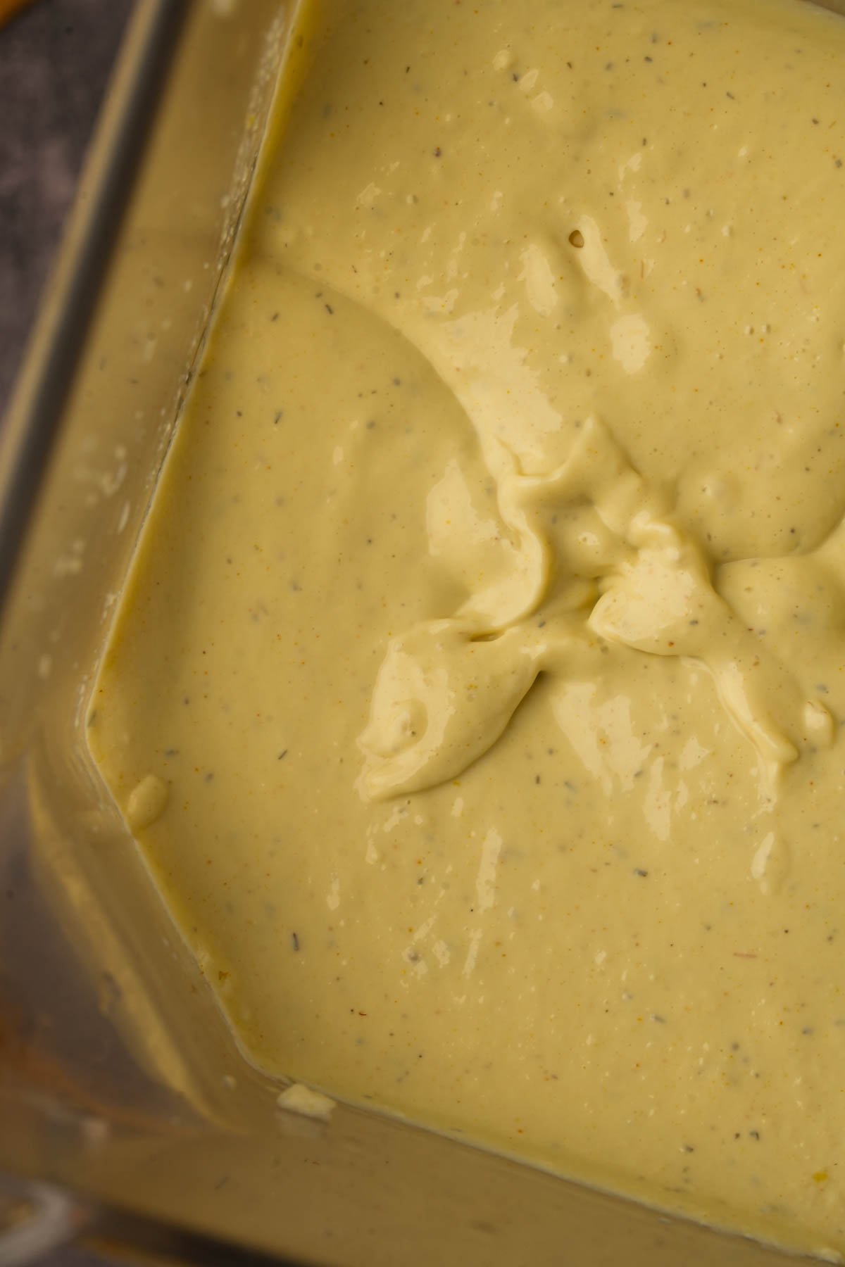 Thick, creamy yellow vegan frittata base or dressing with visible specks, shown in a blender container.