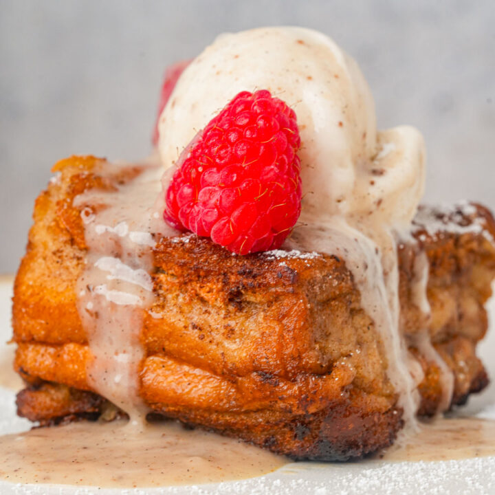 A slice of Hong Kong french toast topped with melted vanilla ice cream, fresh raspberries, and dusted with powdered sugar.