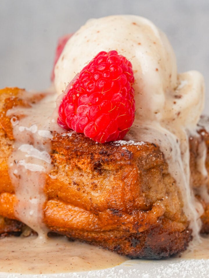 A slice of Hong Kong french toast topped with melted vanilla ice cream, fresh raspberries, and dusted with powdered sugar.