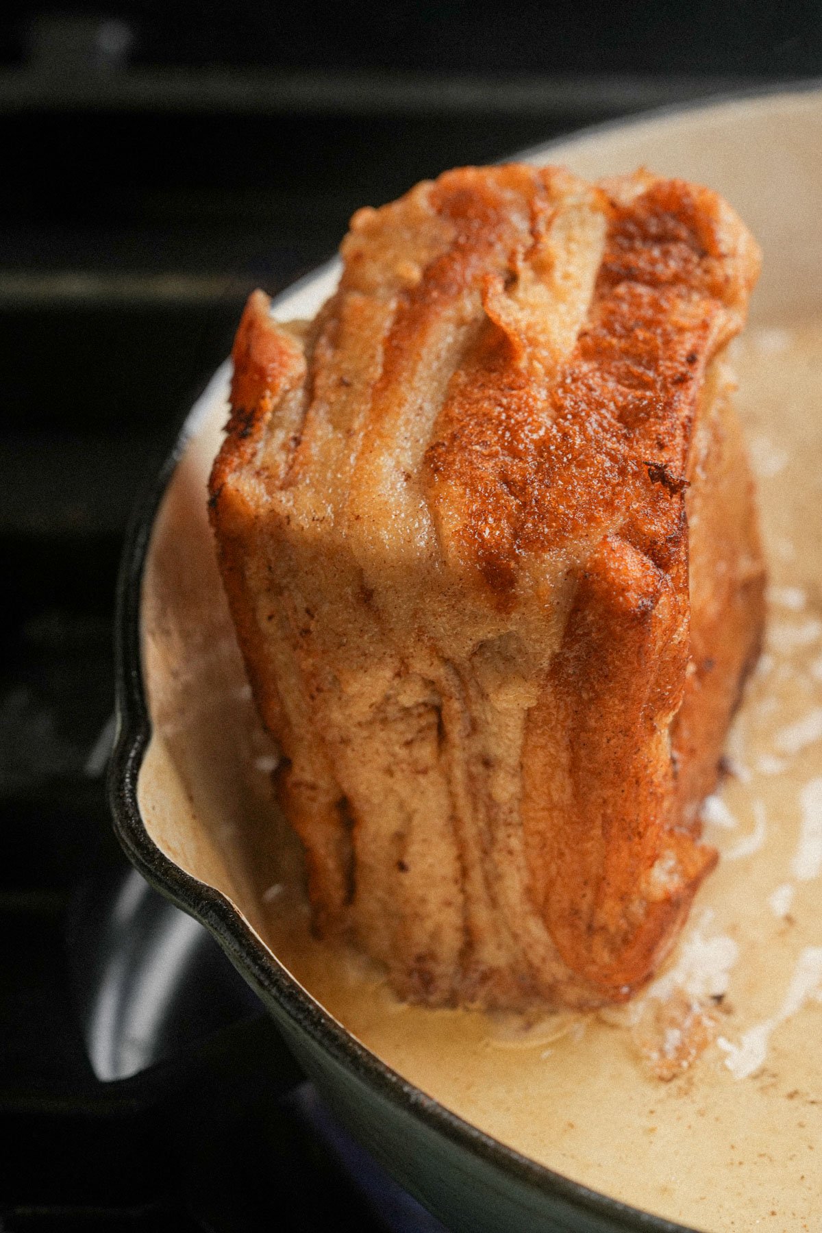 A browned, thick piece of Hong Kong french toast stands upright in a cast iron skillet with oil at the bottom of the pan.