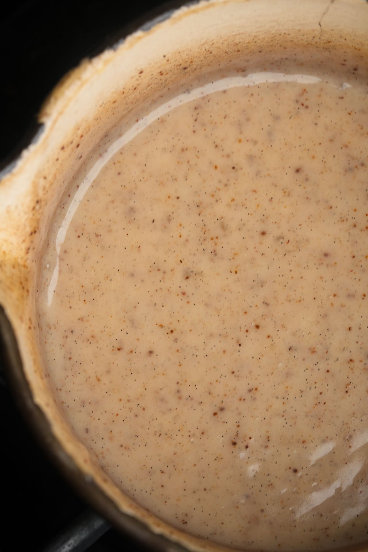 A pot filled with a creamy, condensed coconut milk sauce speckled with small flecks of vanilla.