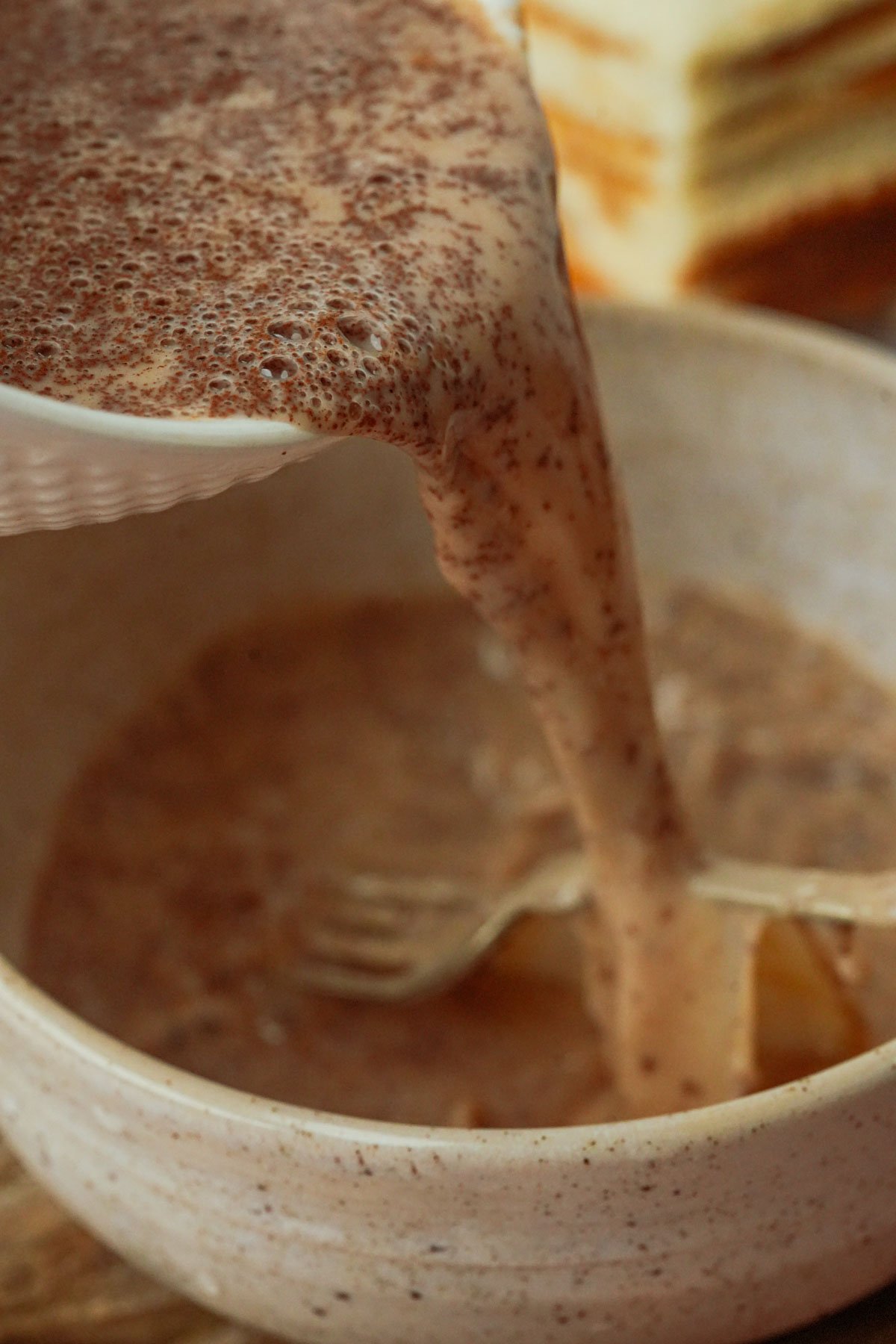 A close-up of a thick, cinnamon speckled Hong Kong french toast batter being poured from a bowl into another bowl with a fork inside.