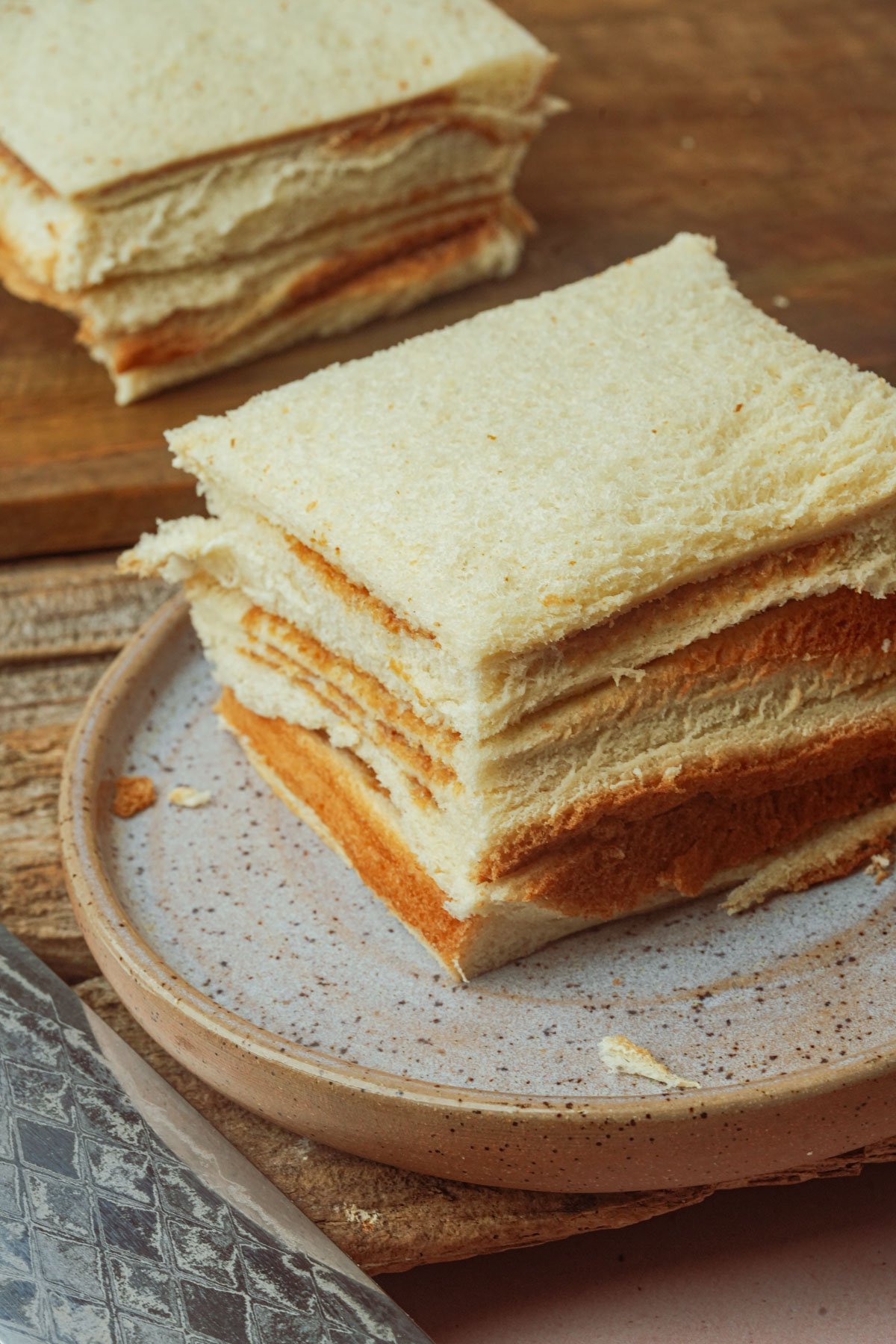 A stack of crustless white bread slices arranged on a ceramic plate for making Hong Kong french toast.