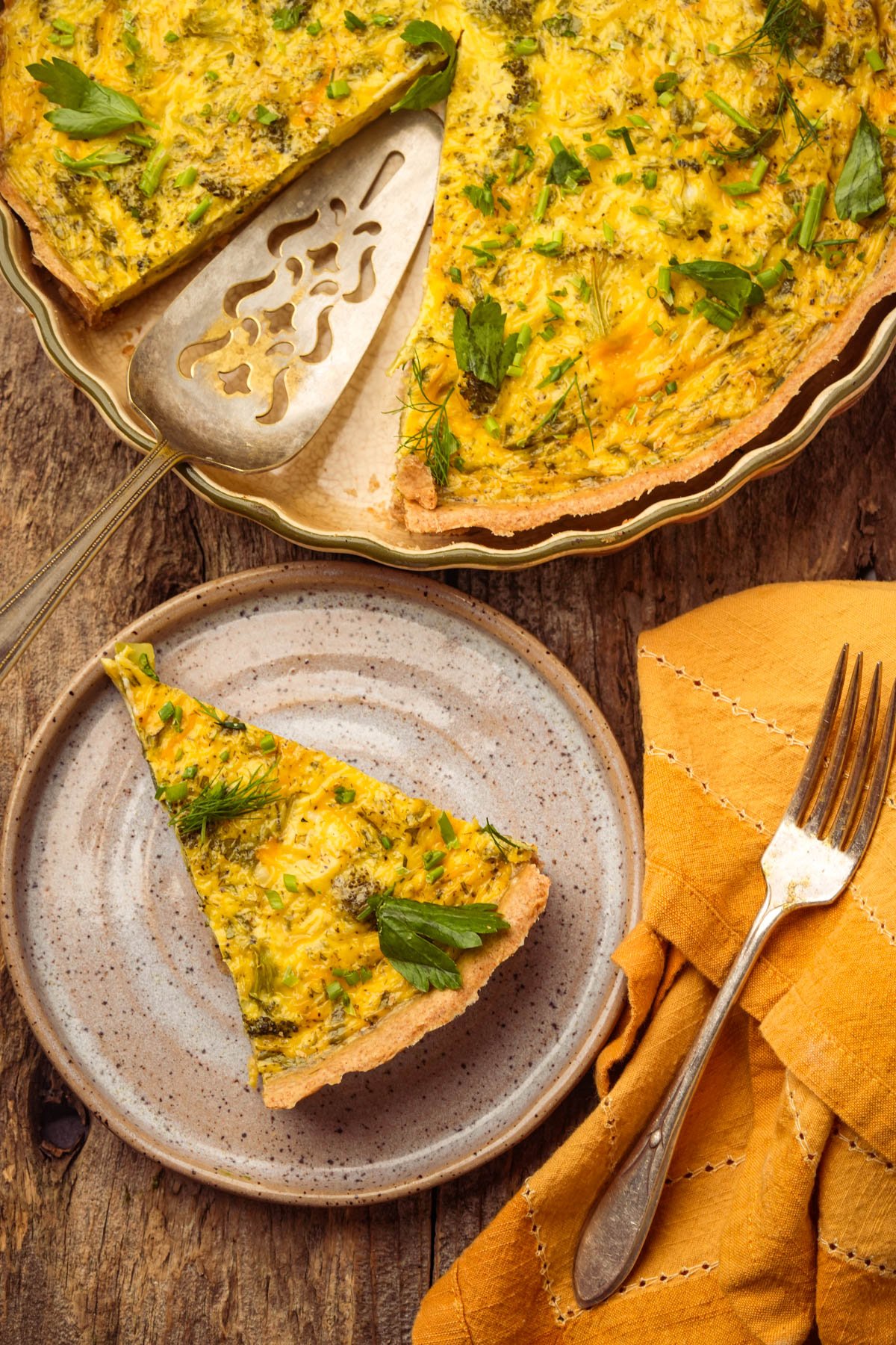 A slice of vegan quiche on a plate with a fork, next to a larger quiche in a pie dish on a wooden table.